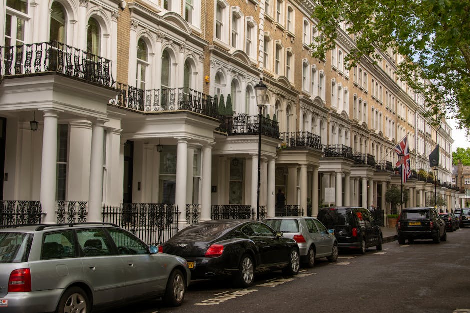 Black and white photograph of a row of multi-storey residential buildings with a traditional London townhouse façade, featuring multiple windows, decorative cornices, and small balconies. The buildin
